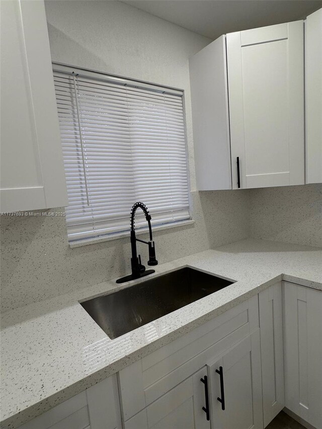 kitchen featuring white cabinetry, light stone countertops, and sink