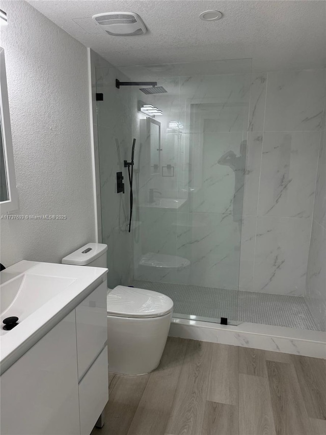 bathroom with a tile shower, wood-type flooring, vanity, toilet, and a textured ceiling