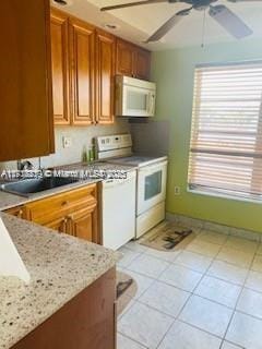 kitchen with light tile patterned flooring, sink, ceiling fan, light stone countertops, and white appliances