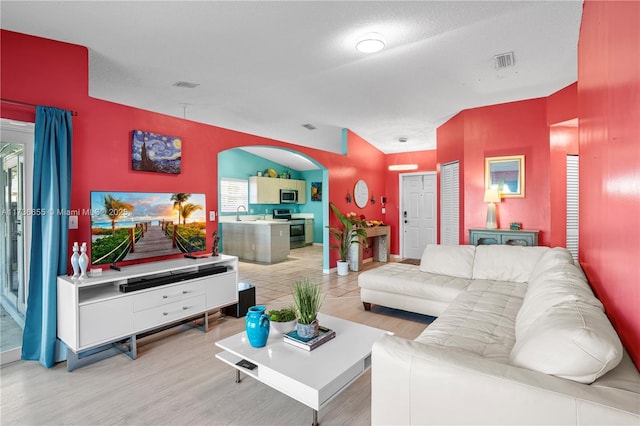 living room featuring lofted ceiling, sink, and light hardwood / wood-style floors