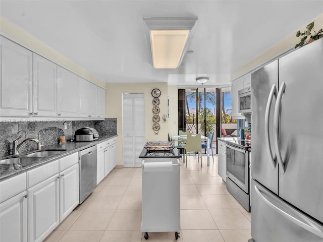 kitchen featuring light tile patterned floors, stainless steel appliances, a sink, white cabinets, and backsplash