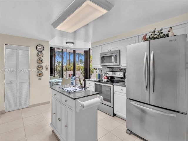 kitchen with stainless steel appliances, dark countertops, light tile patterned flooring, and white cabinets