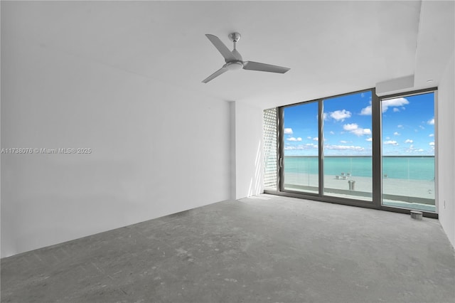 empty room featuring a water view, ceiling fan, expansive windows, and concrete floors