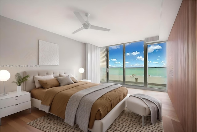 bedroom featuring a water view, light hardwood / wood-style flooring, expansive windows, ceiling fan, and access to exterior