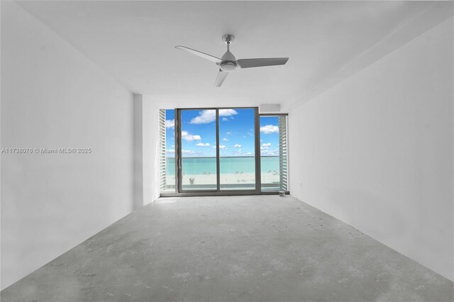 unfurnished room featuring expansive windows, a water view, concrete floors, and ceiling fan