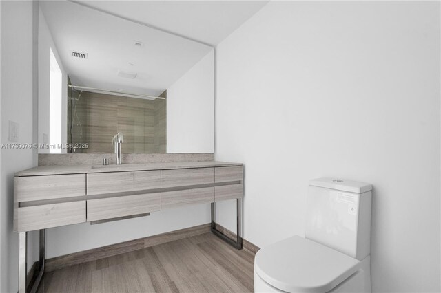 bathroom with hardwood / wood-style flooring, vanity, toilet, and a shower with door