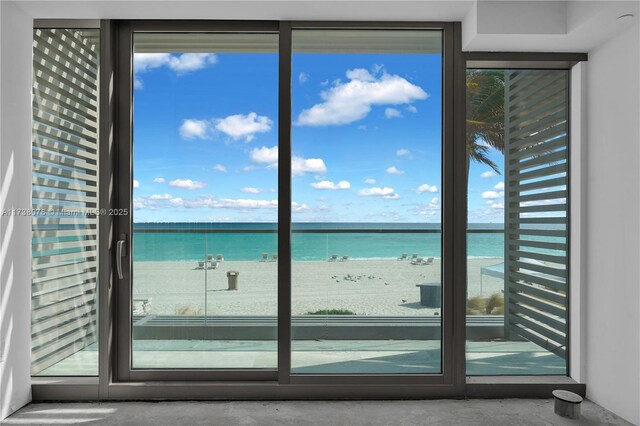 doorway to outside with a water view, a beach view, and concrete floors