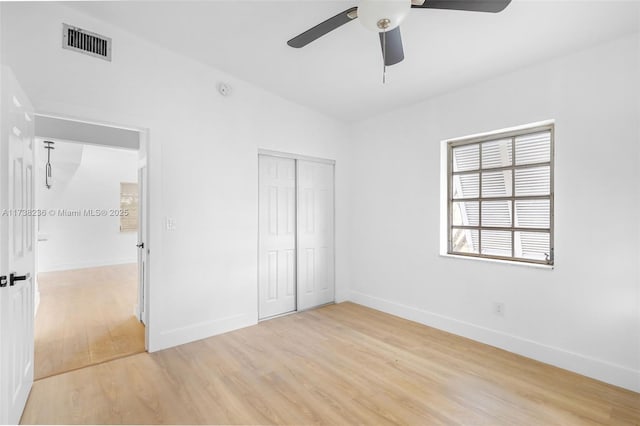 unfurnished bedroom with baseboards, light wood-style flooring, visible vents, and a closet