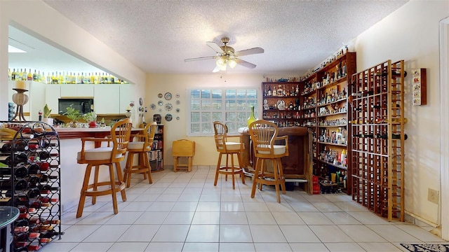 wine cellar with light tile patterned flooring, indoor bar, ceiling fan, and a textured ceiling