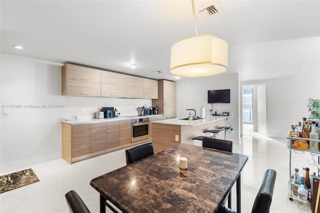 kitchen featuring decorative light fixtures, sink, a kitchen bar, stainless steel oven, and a center island with sink