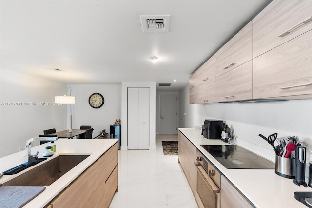 kitchen featuring black electric stovetop, sink, hanging light fixtures, and light brown cabinets