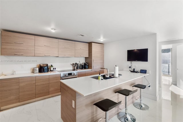 kitchen with black electric stovetop, sink, a kitchen breakfast bar, and stainless steel oven