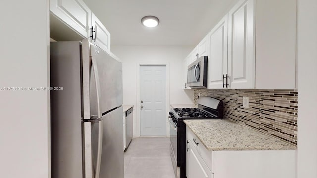 kitchen featuring light tile patterned floors, appliances with stainless steel finishes, tasteful backsplash, light stone counters, and white cabinets