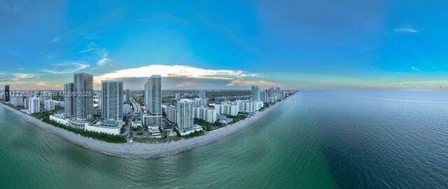 aerial view at dusk featuring a water view and a view of the beach