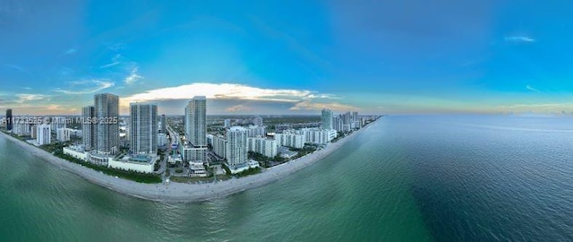 aerial view at dusk featuring a view of city, a water view, and a beach view