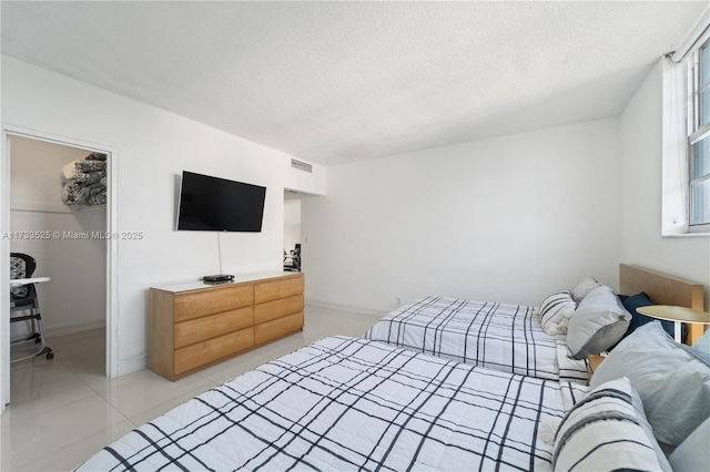 bedroom featuring a textured ceiling, light tile patterned flooring, visible vents, a spacious closet, and a closet