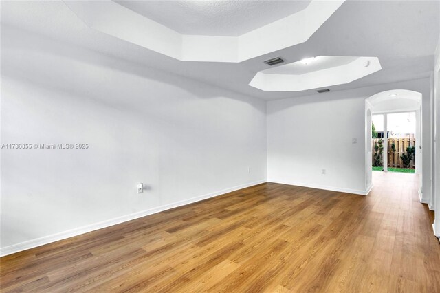 empty room featuring a raised ceiling, wood-type flooring, and a textured ceiling