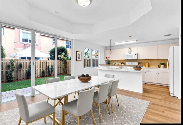 dining space with a raised ceiling and light wood-type flooring