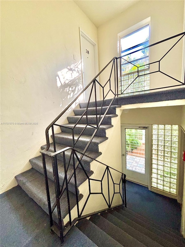 stairway featuring a healthy amount of sunlight, carpet, and a high ceiling