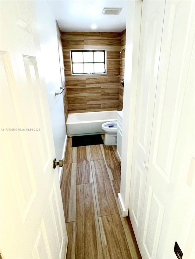 bathroom with wood-type flooring, tiled shower / bath, and toilet