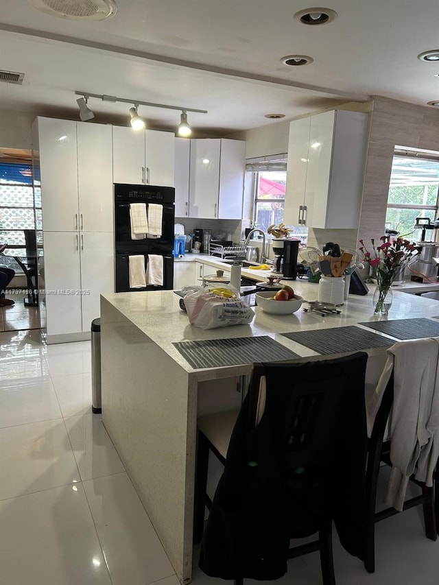 kitchen with white cabinetry, black double oven, and light tile patterned floors