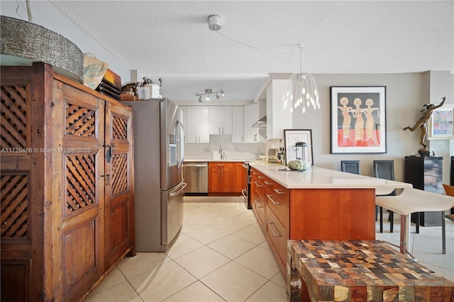 kitchen featuring appliances with stainless steel finishes, pendant lighting, white cabinets, light tile patterned floors, and a textured ceiling