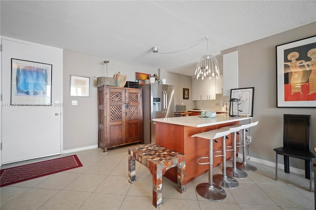 kitchen featuring a breakfast bar area, hanging light fixtures, light tile patterned floors, kitchen peninsula, and stainless steel refrigerator with ice dispenser