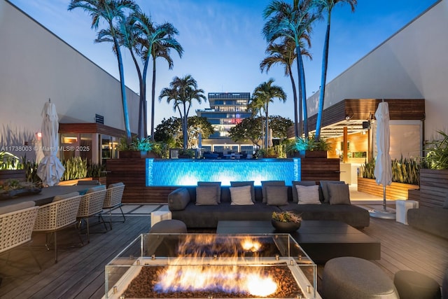 pool at dusk featuring a wooden deck and an outdoor living space with a fire pit