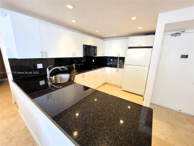 kitchen with tasteful backsplash, dark stone counters, freestanding refrigerator, black microwave, and a sink