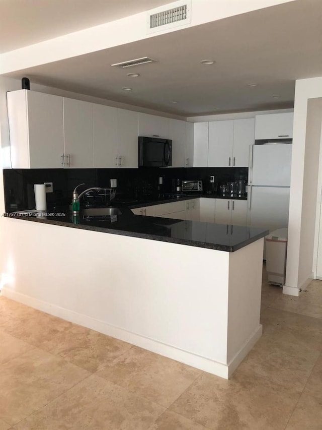 kitchen with dark countertops, freestanding refrigerator, a sink, black microwave, and a peninsula