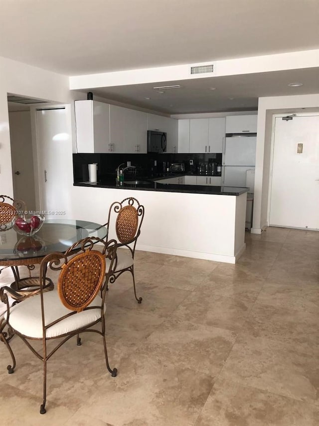 kitchen with black microwave, visible vents, dark countertops, a peninsula, and white cabinetry