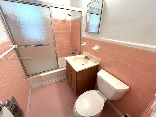 full bathroom featuring bath / shower combo with glass door, tile walls, vanity, and toilet