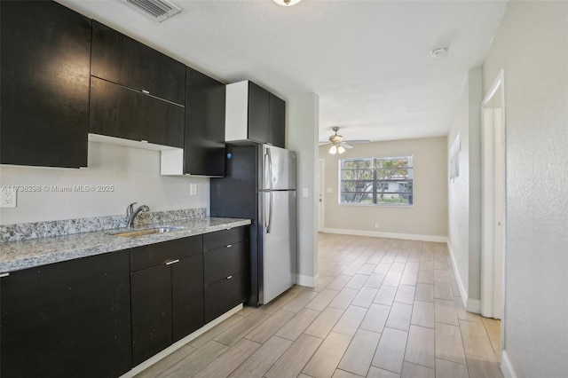 kitchen featuring sink, stainless steel fridge, light stone countertops, and ceiling fan