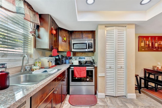 kitchen with appliances with stainless steel finishes, light stone countertops, sink, and backsplash