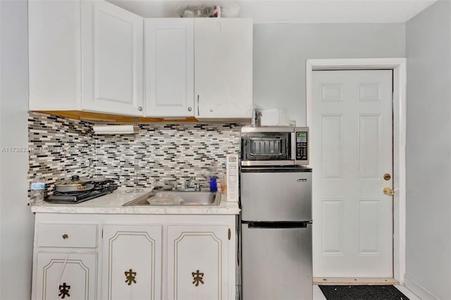 kitchen with appliances with stainless steel finishes, sink, white cabinets, and backsplash