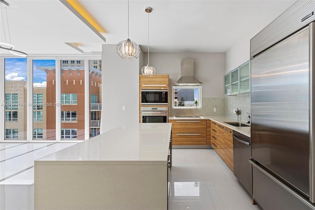 kitchen with wall chimney exhaust hood, sink, tasteful backsplash, built in appliances, and a kitchen island