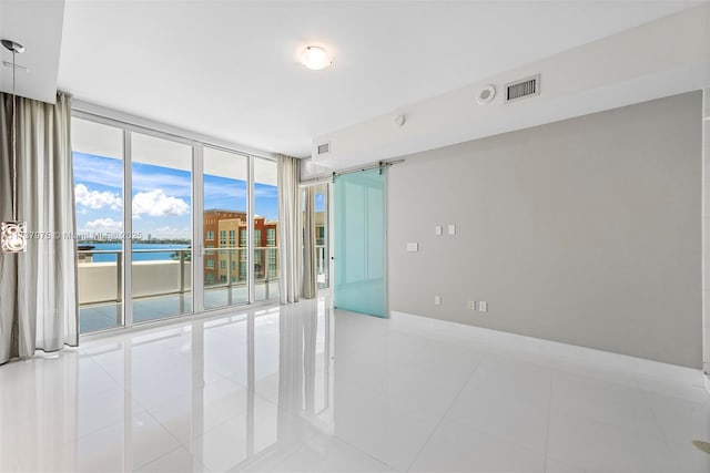 spare room with light tile patterned floors, floor to ceiling windows, a barn door, and a water view