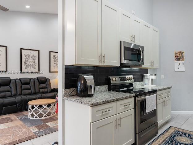 kitchen with white cabinetry, backsplash, light tile patterned floors, light stone counters, and stainless steel appliances