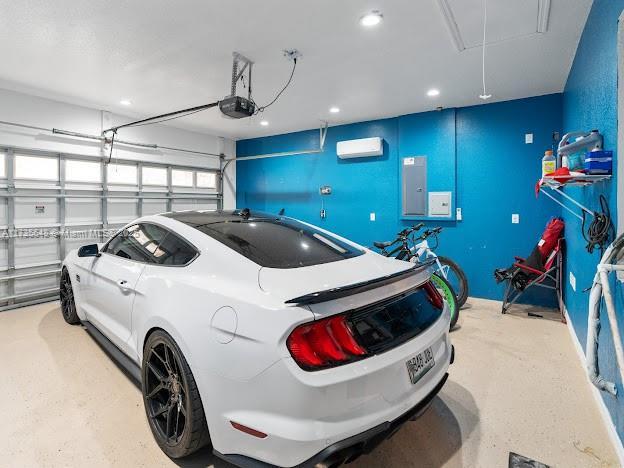 garage featuring a wall mounted air conditioner, a garage door opener, and electric panel