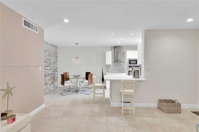 kitchen featuring a breakfast bar area, appliances with stainless steel finishes, kitchen peninsula, wall chimney range hood, and white cabinets