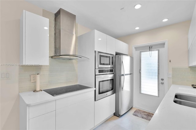 kitchen featuring sink, white cabinetry, tasteful backsplash, appliances with stainless steel finishes, and wall chimney range hood