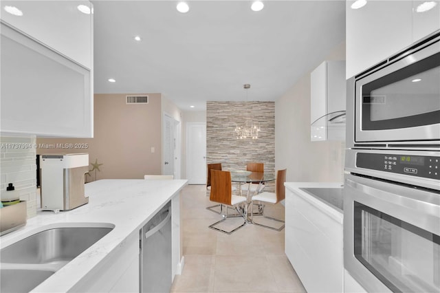 kitchen featuring light tile patterned flooring, light stone counters, decorative light fixtures, stainless steel appliances, and white cabinets