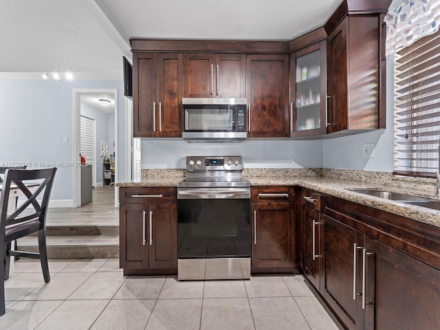 kitchen with light stone countertops, light tile patterned floors, dark brown cabinets, and stainless steel appliances