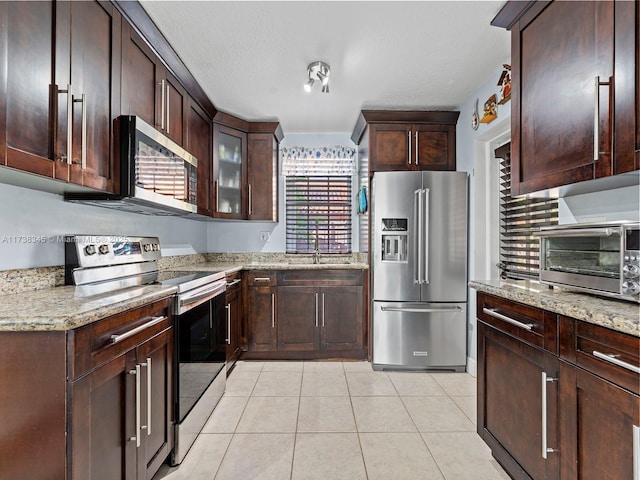 kitchen with stainless steel appliances, dark brown cabinetry, light stone countertops, a textured ceiling, and light tile patterned flooring