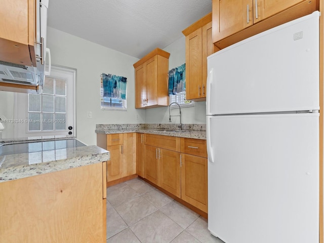 kitchen with sink, white refrigerator, light tile patterned floors, light stone counters, and a textured ceiling