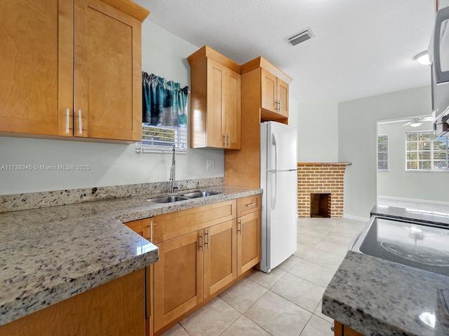 kitchen with sink, white refrigerator, light tile patterned floors, ceiling fan, and a brick fireplace