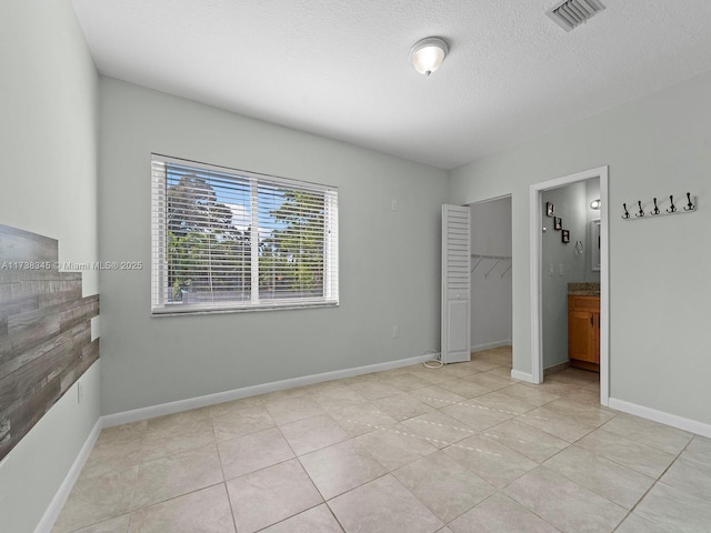 unfurnished bedroom with ensuite bathroom, light tile patterned floors, a textured ceiling, and a closet