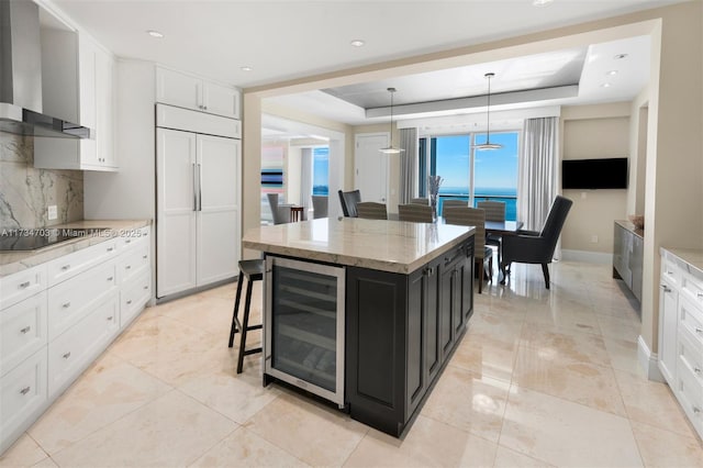 kitchen featuring beverage cooler, a center island, paneled built in fridge, black electric cooktop, and wall chimney exhaust hood