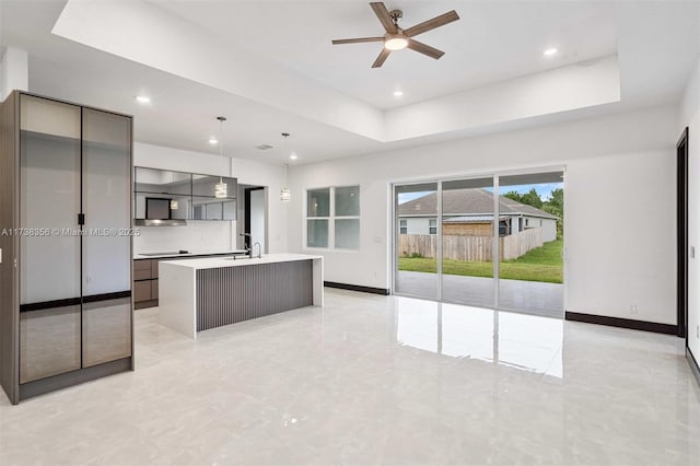 kitchen with a center island with sink, a sink, light countertops, a raised ceiling, and modern cabinets