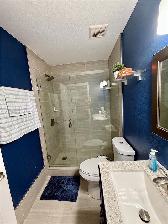 bathroom featuring vanity, toilet, a shower with shower door, and a textured ceiling